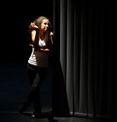 Leila Anis devant un rideau noir , semble  se moquer de quelqu'un ou de quelqu'un ou de quelque chose 