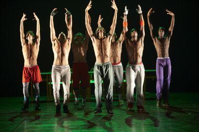 Vêtus de pantalons de jogging ou de short, les danseurs, torse-nu, lèvent les bras tous ensemble.