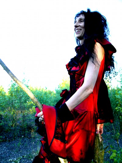 Myriam Pellicane dans une splendide robe rouge à volants tient son balais de sorcière à la main 
