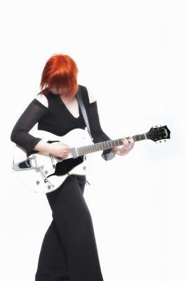 l'affiche d'Evelyne Gallet. Vétûe d'une longue robe noire ; elle tient une guitare blanche à la main. Ses cheveux orange apportent une touche plus contemporaine à sa tenue vestimentaire.